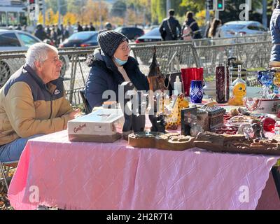 Coppia di mezza età seduta al loro stallo del mercato delle pulci. La loro merce è visualizzata su un tavolo basso e sono in attesa per i clienti. Foto Stock