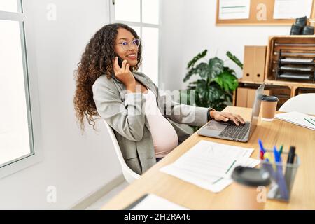 Giovane donna latina incinta che parla sullo smartphone che lavora in ufficio Foto Stock