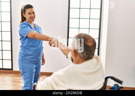 Uomo anziano seduto su sedia a rotelle e infermiera geriatrica che fa accordo di scuotimento della mano, ringraziando per l'aiuto Foto Stock