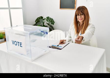 Giovane donna ispanica sorridente fiducioso di tenere il voto e scrivere negli appunti presso l'istituto elettorale Foto Stock