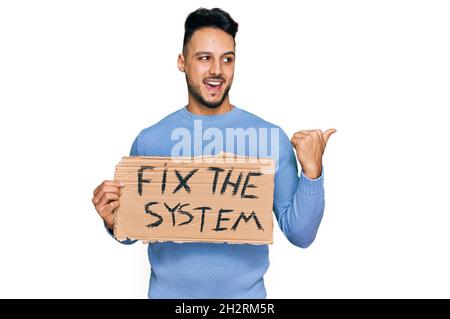 Giovane uomo arabo che regge fissare il sistema banner cartone puntando il pollice verso il lato sorridendo felice con bocca aperta Foto Stock