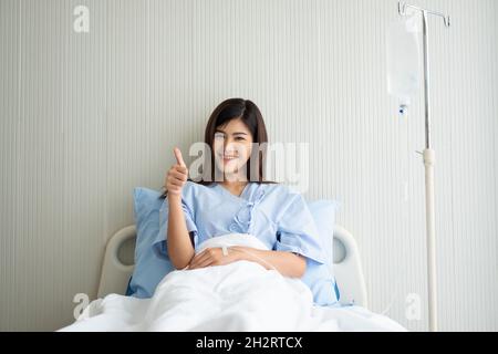 Felice paziente asiatico femmina sorridente, si trova sul letto, e solleva il pollice fino a mostrare fiducia nel trattamento. Concetto di credere in trattamento e assicurazione Foto Stock