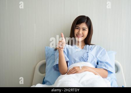 Felice paziente asiatico femmina sorridente, si trova sul letto, e solleva il pollice fino a mostrare fiducia nel trattamento. Concetto di credere in trattamento e assicurazione Foto Stock