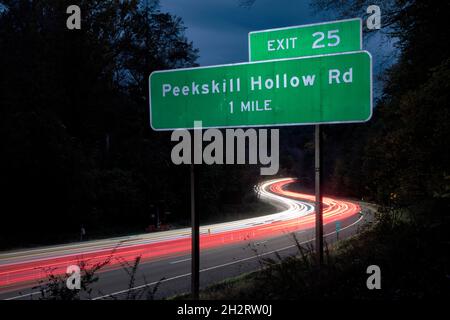 Il traffico dell'ora di punta è offuscato da una lenta velocità dell'otturatore della fotocamera sulla Taconic state Parkway nella contea di Putnam, New York. Segnale di uscita Peekskill Hollow Road. Foto Stock