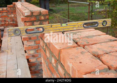 Muratura con livella a spirito per controllare il nuovo muro della casa del mattone rosso. Bricklaying di base sul luogo di costruzione della casa Foto Stock