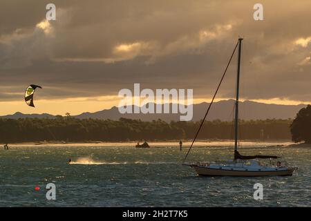 Un kite surfer e uno yacht in acqua al tramonto. Monte Maunganui, Nuova Zelanda Foto Stock