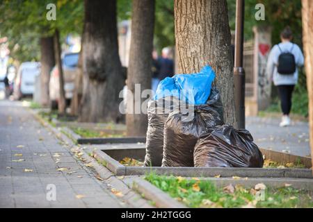 Mucchio di sacchi di rifiuti neri pieno di lettiera sinistra per pick up sul lato della strada. Concetto di smaltimento rifiuti. Foto Stock