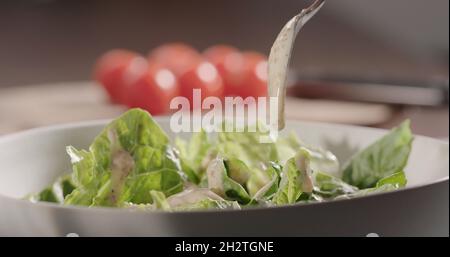 versare il condimento alla noce sulle foglie di romaina in un recipiente bianco, facendo l'insalata, foto larga Foto Stock