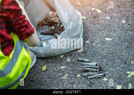 pulizia volontaria della siringa usata in posizione di parcheggio e in piedi da un mazzetto di sacco per rifiuti Foto Stock