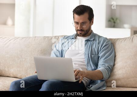 Concentrato giovane uomo in occhiali che lavora su un portatile. Foto Stock