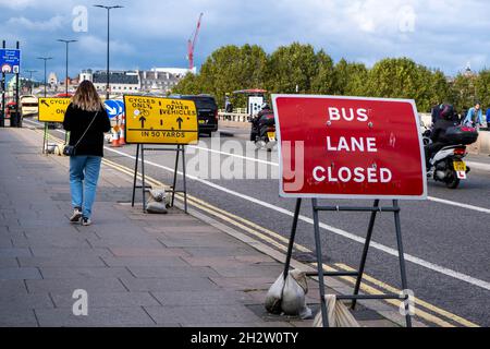 Giovane donna vestita casualmente camminando da solo lungo Waterloo Bridge London England UK passando le indicazioni stradali e il traffico Foto Stock