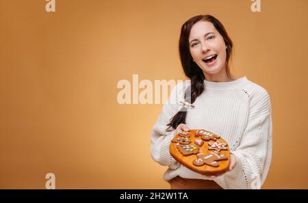 Donna felice confettatrice che tiene vassoio di legno con biscotti di pan di zenzero. Foto Stock