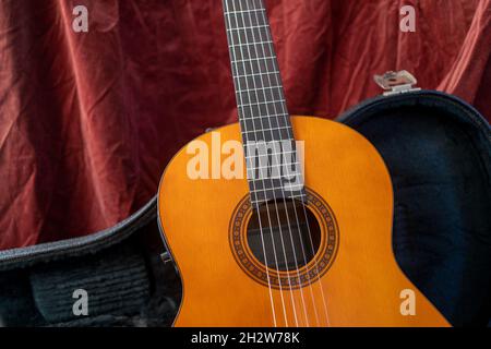 Chitarra classica su sfondo rosso in custodia rigida. Concetto di chitarra acustica. Foto Stock