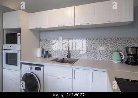 Interni moderni di elegante cucina bianca con elettrodomestici. Lavatrice. Foto Stock