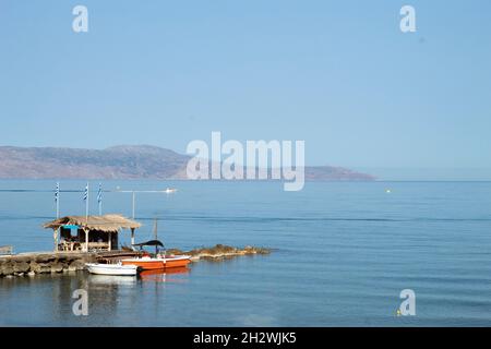 Bella Agia Marina resort, Creta, Grecia tranquillo mare con escursioni barche ormeggiate in un piccolo molo aspetto paesaggio con cielo blu e copia spa Foto Stock