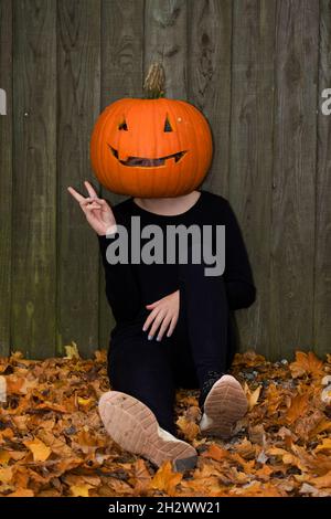 La ragazza sedette sulle foglie con una zucca scolpita sulla testa Foto Stock