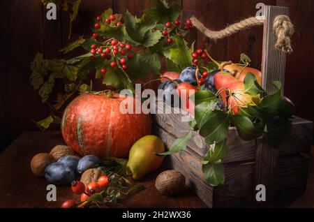 pere e prugne con un ramo di rosa selvaggia in una scatola di legno su sfondo di legno scuro in stile rustico Foto Stock