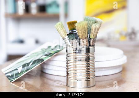 Una lattina di metallo con pennelli di vernice e una tela con un'immagine di un mostera. Foto Stock