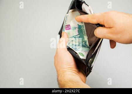 Un vecchio portafoglio in mano agli uomini con denaro russo, primo piano, sfondo grigio Foto Stock