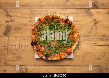 Serrana pizza a crosta sottile con prosciutto spagnolo e rucola cotta in forno a pietra e presentata su un tavolo di legno Foto Stock