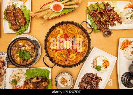 Immagine vista dall'alto di piatti fusion asiatici e spagnoli, paella di pesce, nocciola con riso, croccanti involtini di pesce, spiedini di maiale arrosto, stufato di maiale Foto Stock