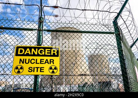 Un cartello giallo di pericolo sulla recinzione di sicurezza di una centrale nucleare con due torri di raffreddamento sullo sfondo. Foto Stock