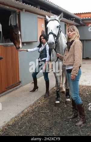 le jockey femminili nell'arena preparano i loro cavalli per uscire per un trotto Foto Stock