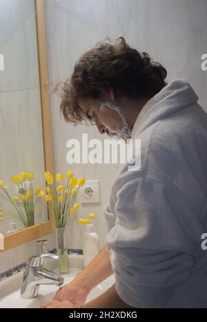 Giovane uomo che lava le mani dopo aver applicato la schiuma da barba al viso. Beauty Home Spa concetto. Foto Stock
