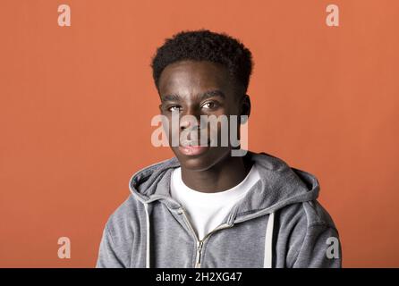 Bel giovane uomo nero in un ritratto con cappuccio grigio e spalle studio, mentre guarda con cura la fotocamera con un sorriso tranquillo Foto Stock