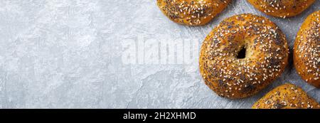 Varietà di bagel freschi a grani interi con semi di papavero, semi di sesamo su un calcestruzzo leggero o sfondo di pietra. Messa a fuoco selettiva. Vista dall'alto. Spazio di copia. Foto Stock