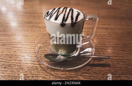 Cappuccino a strati in una tazza di vetro trasparente con cioccolato versato sulla parte superiore Foto Stock