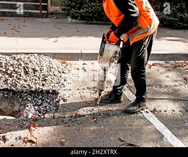 I lavoratori rimuovono uno strato di asfalto vecchio con un martello pneumatico in autunno. Lavori di costruzione su strada. Foto Stock