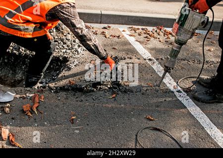 I lavoratori rimuovono uno strato di asfalto vecchio con un martello pneumatico in autunno. Lavori di costruzione su strada. Foto Stock