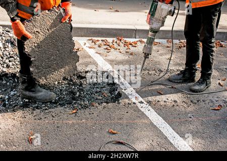 I lavoratori rimuovono uno strato di asfalto vecchio con un martello pneumatico in autunno. Lavori di costruzione su strada. Foto Stock