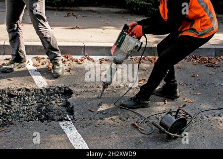 I lavoratori rimuovono uno strato di asfalto vecchio con un martello pneumatico in autunno. Lavori di costruzione su strada. Foto Stock