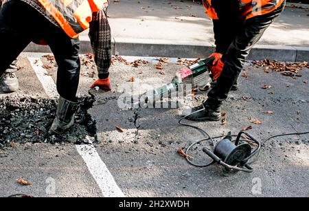 I lavoratori rimuovono uno strato di asfalto vecchio con un martello pneumatico in autunno. Lavori di costruzione su strada. Foto Stock