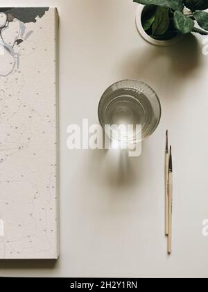 Dipingere la foto con una tela bianca e pennelli su un tavolo di legno bianco con una pianta verde Foto Stock
