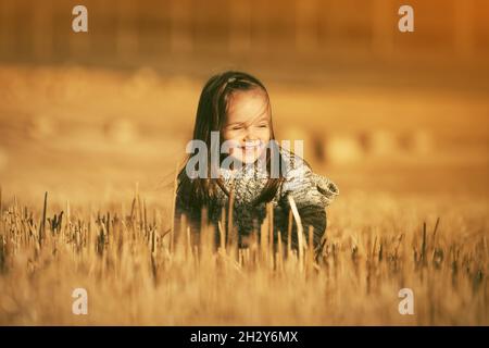 Felice ragazza di due anni in maglia felpa con cappuccio camminare in estate campo raccolto Foto Stock