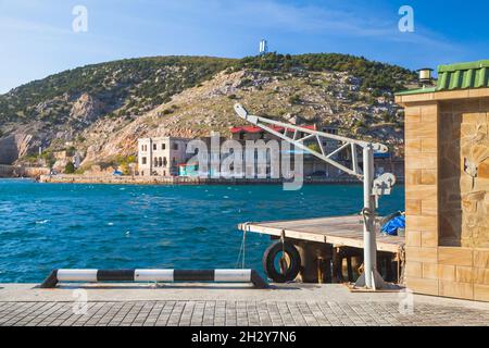 Piccola gru per il sollevamento di imbarcazioni. Baia di Balaklava, paesaggio estivo. Si tratta di un insediamento sulla penisola di Crimea e parte della città di Sevastopol Foto Stock