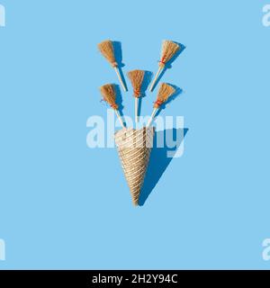 Cinque piccole scopa che escono da un cono di gelato dorato su sfondo blu pastello. Divertente concetto creativo di Halloween. Disposizione piatta. Foto Stock