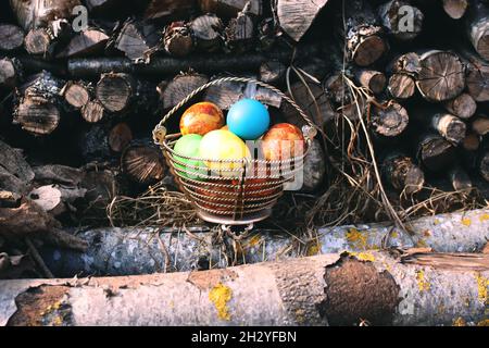 Uova di Pasqua colorate e brillanti in un cestino sul mucchio di legna all'aperto Foto Stock