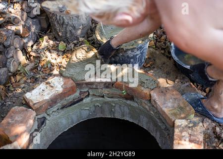 Un lavoratore depone la bocca di un pozzo settico di mattoni. Lavorare con cemento. Foto Stock