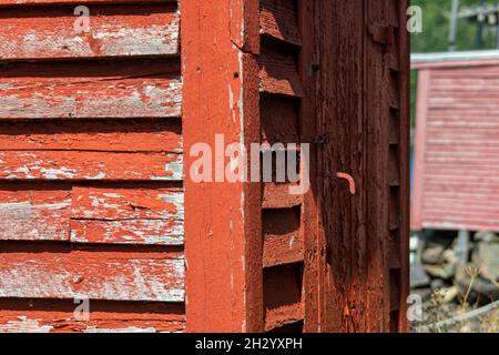 La vista d'angolo esterna di un edificio o capannone rosso brillante d'epoca. La vecchia struttura in legno ha pareti laterali in legno, una maniglia d'epoca Foto Stock