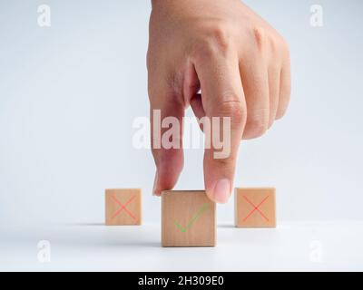 La mano dell'uomo d'affari sceglie l'un blocco di cubo di legno con la destra verde, segno di spunta icona di fronte al segno rosso della croce, segno errato icona blocchi sopra Foto Stock