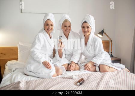 Belle donne in accappatoi sul letto con prodotti cosmetici Foto Stock