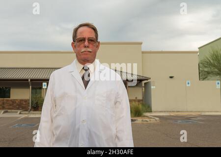 Medico anziano in camice bianco da laboratorio all'aperto di fronte alla clinica. Foto Stock