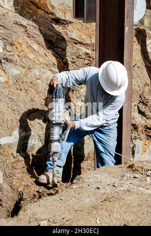 Lavori di costruzione utilizzando un martello per scavare una trincea Foto Stock