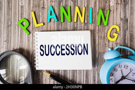 Concetto di pianificazione della successione su blocco note e lettere in legno su tavolo in legno con orologio e lente d'ingrandimento Foto Stock