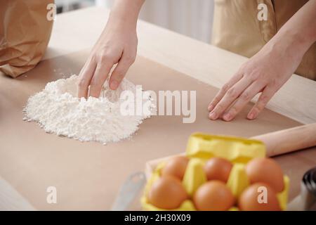 Mani di donna che creano un pozzo al centro della farina per aggiungere l'uovo e mescolare l'impasto Foto Stock