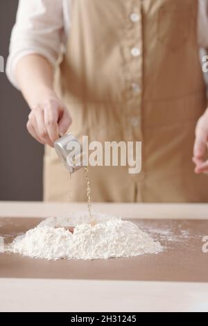 Versare l'acqua di Lye in una pila di farina per mescolare gli ingredienti della pasta per torte alla mooncake Foto Stock